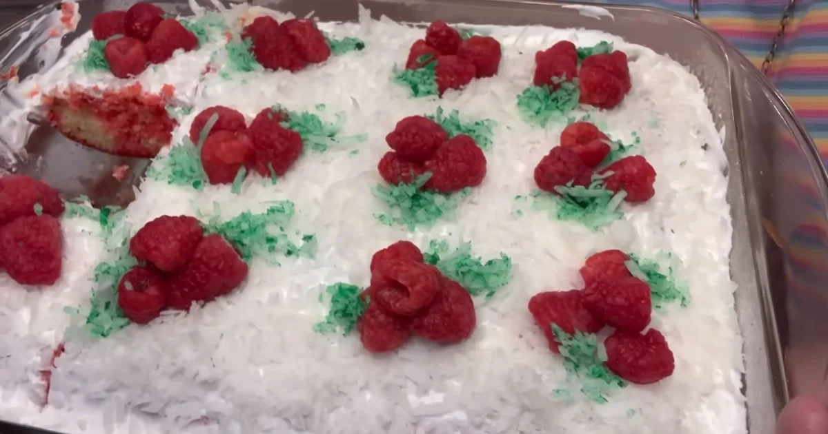 A slice of raspberry zinger poke cake with vibrant raspberry filling, topped with whipped cream and a drizzle of chocolate.