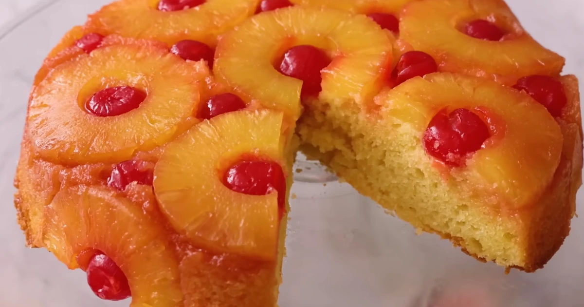 A vibrant pineapple upside down cake shot in a clear glass, showcasing its signature layered effect with golden pineapple juice and red grenadine.