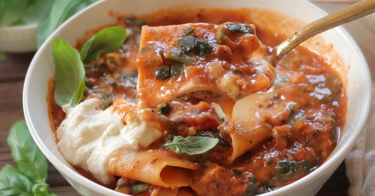 A bowl of Vegan Lasagna Soup garnished with fresh basil and vegan cheese.