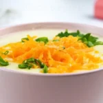 A bowl of creamy 4-Ingredient Potato Soup topped with fresh herbs and a sprinkle of vegan cheese.